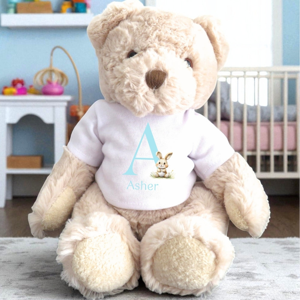 Personalised Luxury Teddy Bear wearing a white T-shirt with a blue initial "A" and bunny design, sitting in a cozy room.