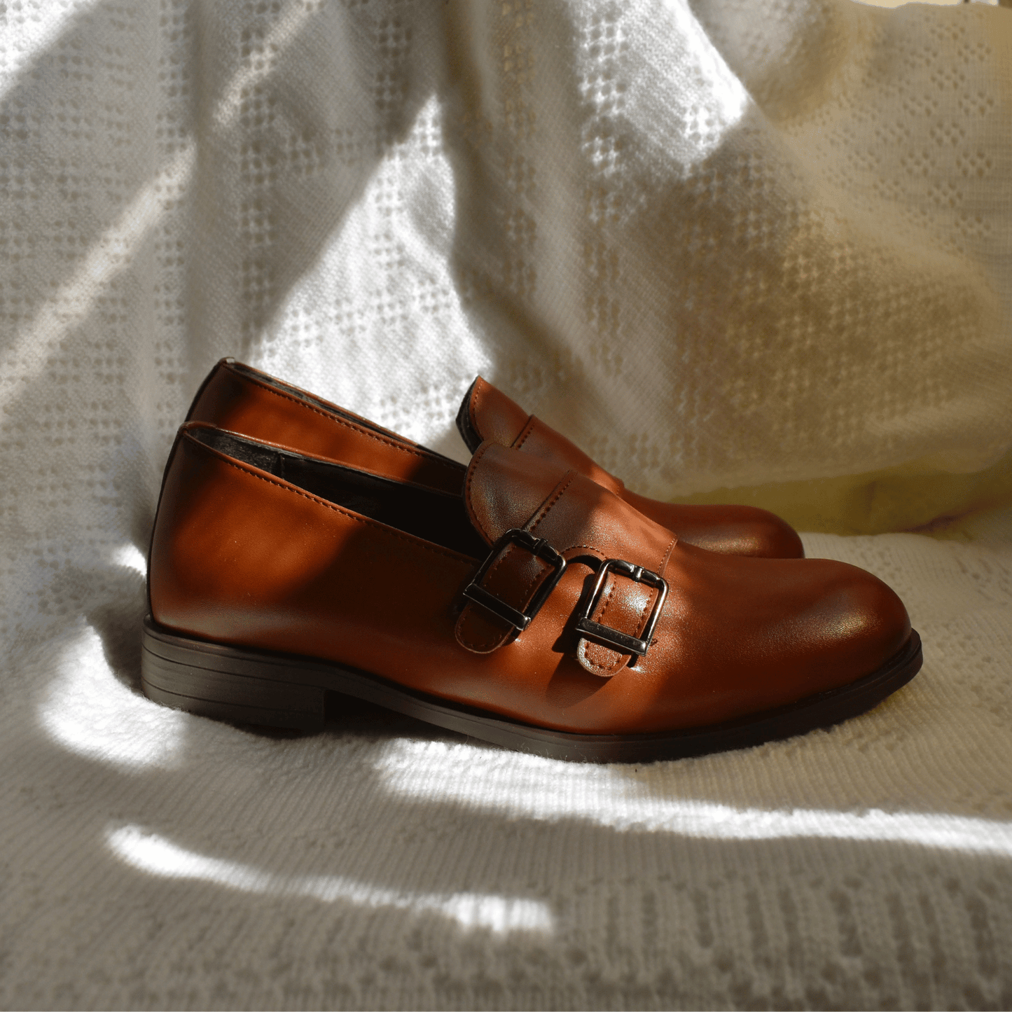 Brown leather Ricky's Shoes with double buckle detail, resting on a textured white surface with soft shadows.