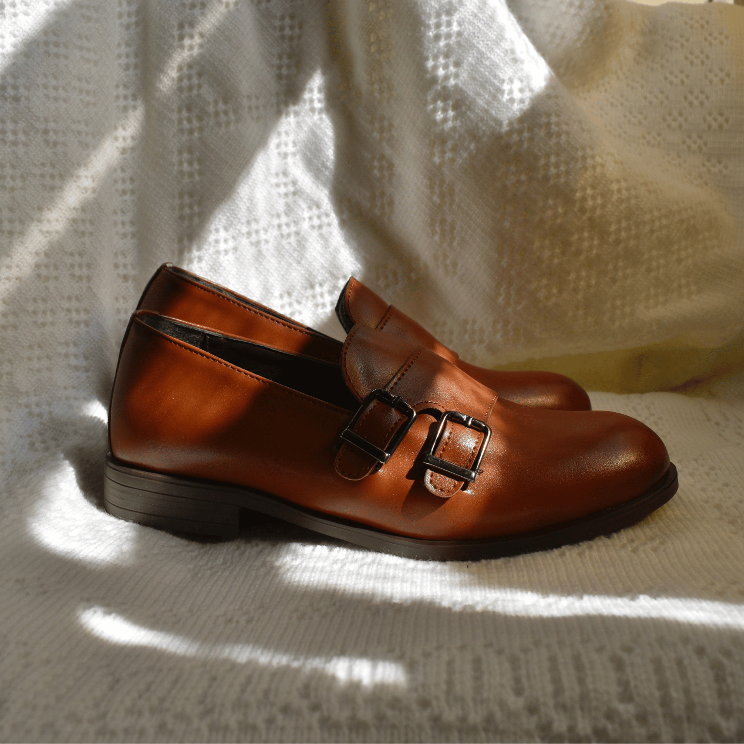 Brown leather Ricky's Shoes with double buckle detail, resting on a textured white surface with soft shadows.