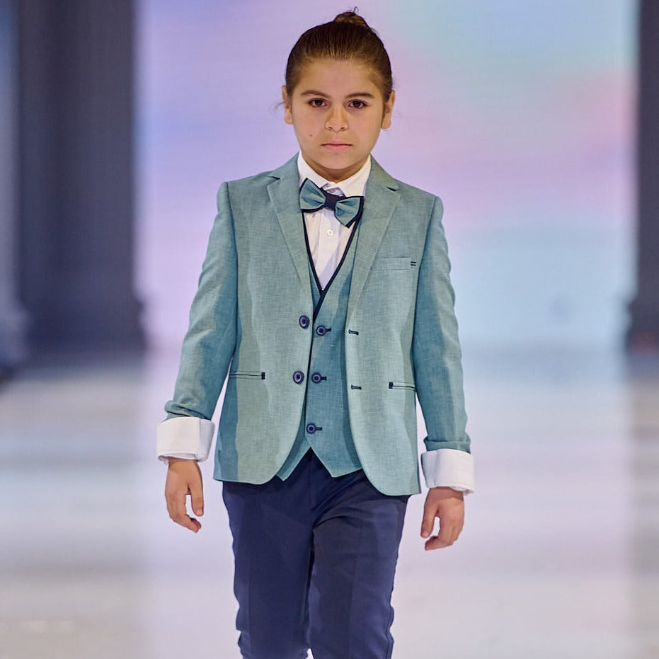 Stylish formal boys suit in light blue with a bow tie, worn by a young boy on a runway.