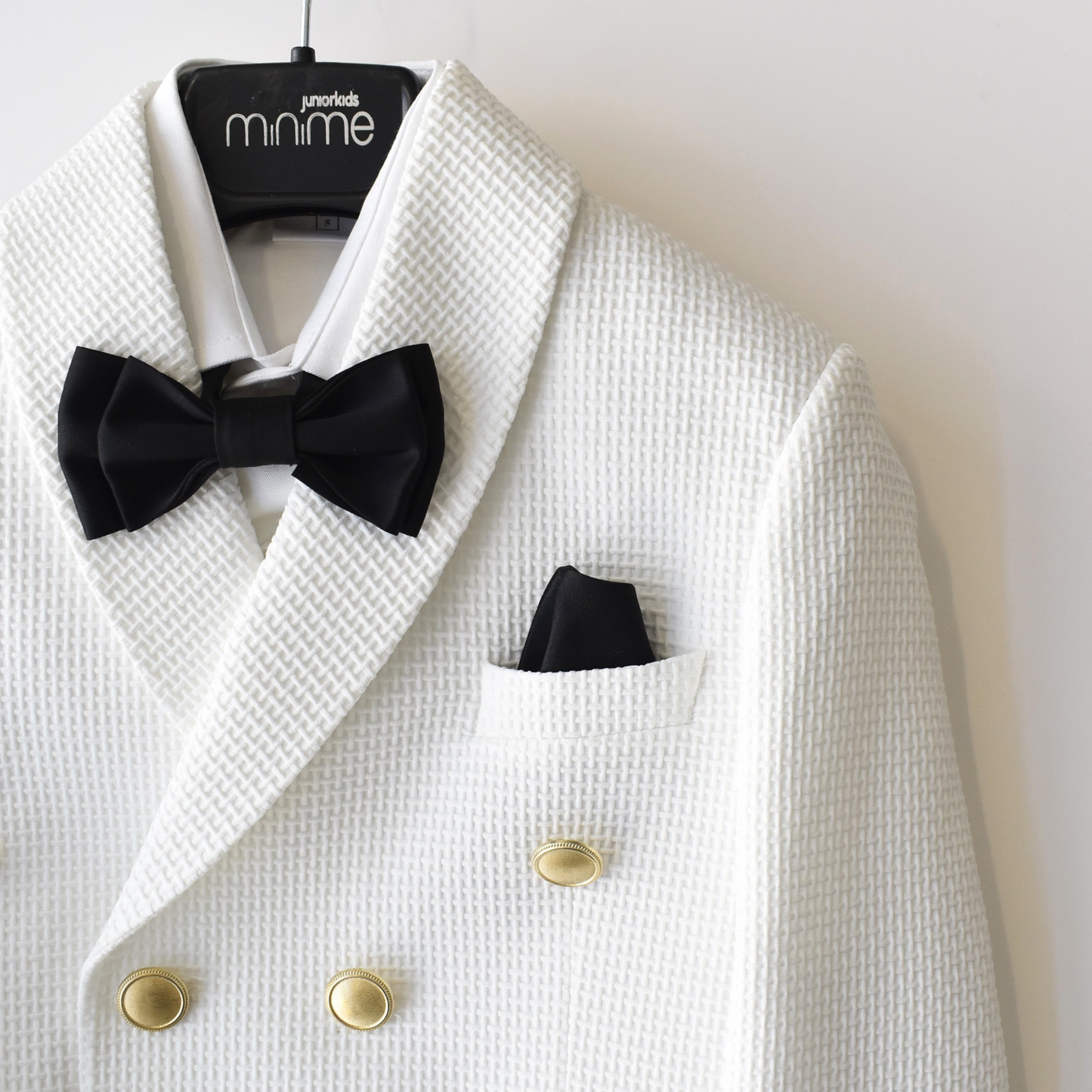 White boys' suit with a textured finish, featuring a double-breasted design, black bow tie, and pocket square.
