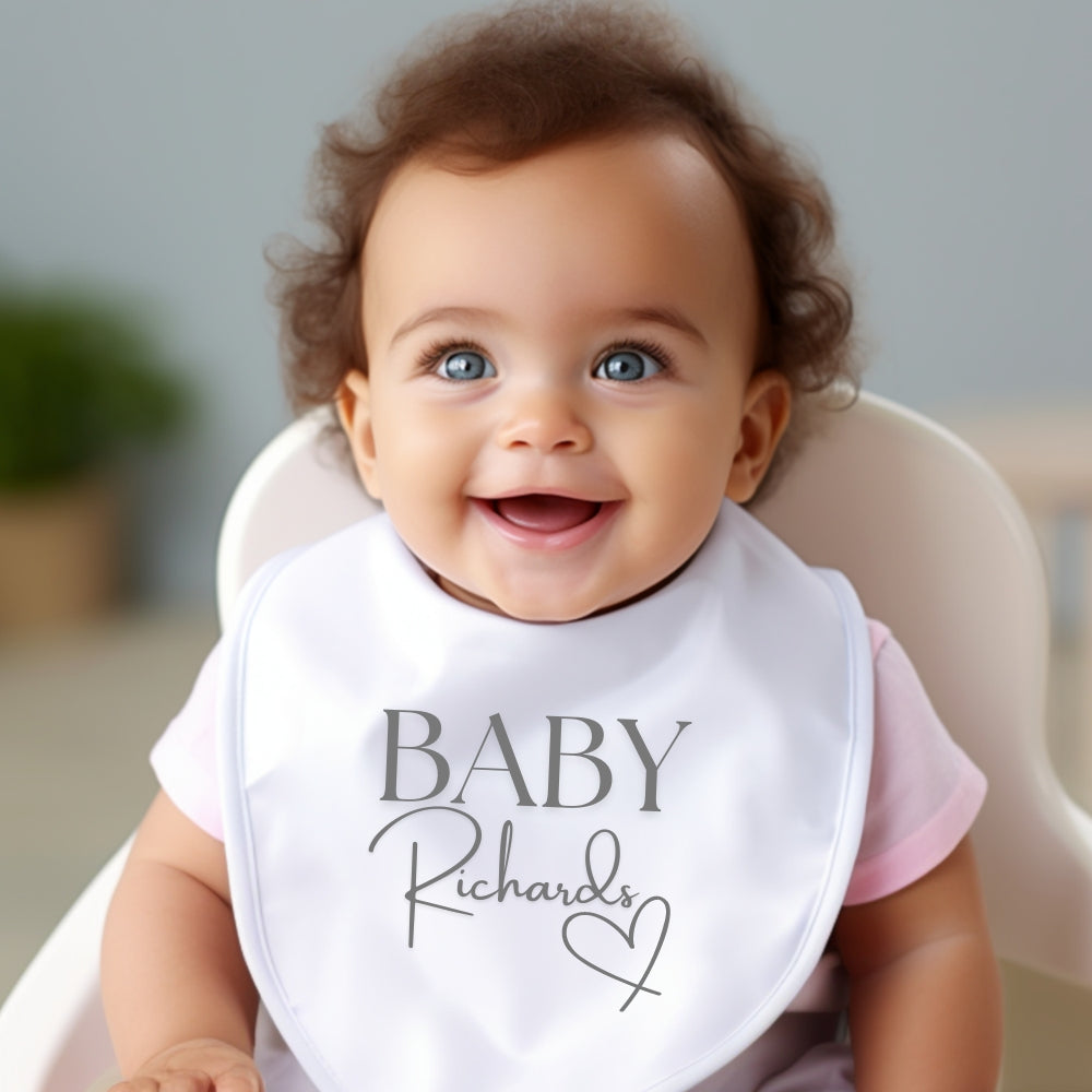 Personalised Surname Heart Baby Outfit featuring a smiling baby wearing a bib with "BABY Richards" design.
