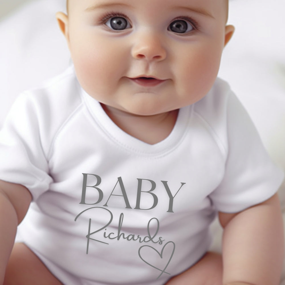 Personalised Surname Heart Baby Outfit featuring a white vest with "BABY Richards" printed in grey.