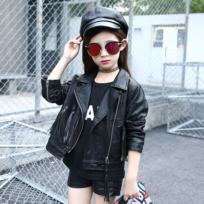 Girls' slim fit short long sleeve tassel jacket in black, styled with sunglasses, choker, and cap, set in an urban environmen
