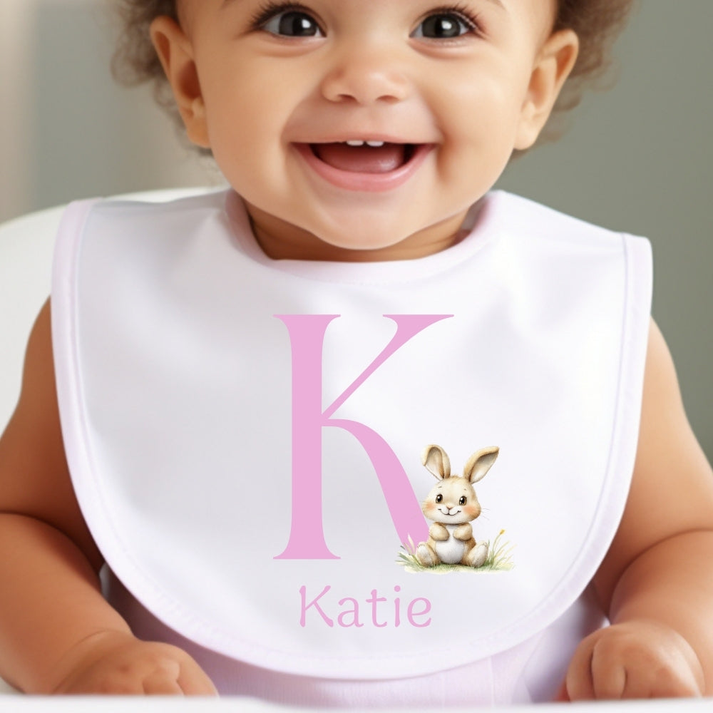 Personalised Pink Initial Bunny Baby Outfit featuring a smiling baby wearing a bib with a pink letter 'K' and bunny design.