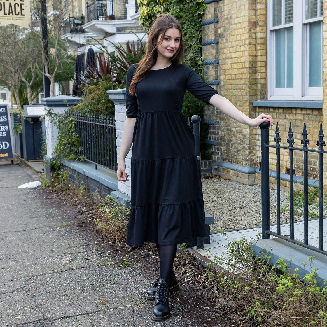 The Midi Breastfeeding Dress - Beth Black Cotton features a model in a black, tiered dress with three-quarter sleeves, styled