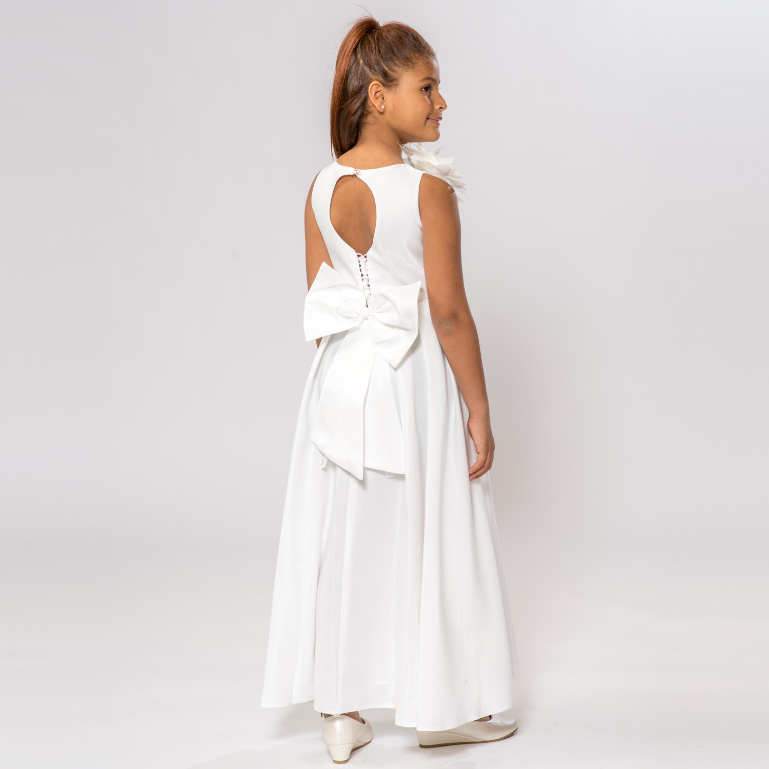 A-line dress for girls in white with a large bow at the back and a floral accent on the shoulder. Elegant and stylish design.