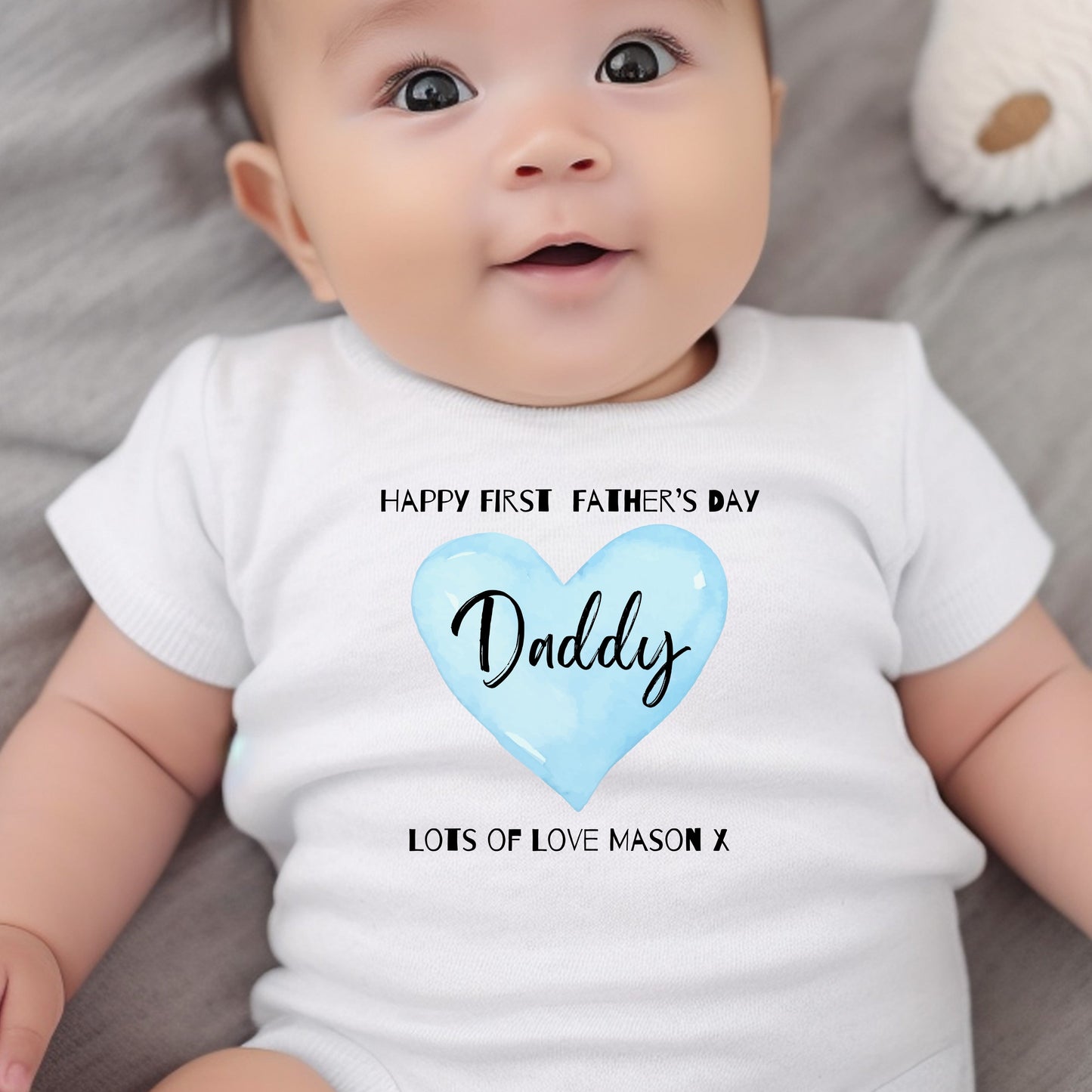Personalised blue Happy First Father's Day baby outfit featuring a white vest with a heart design and text for "Daddy."