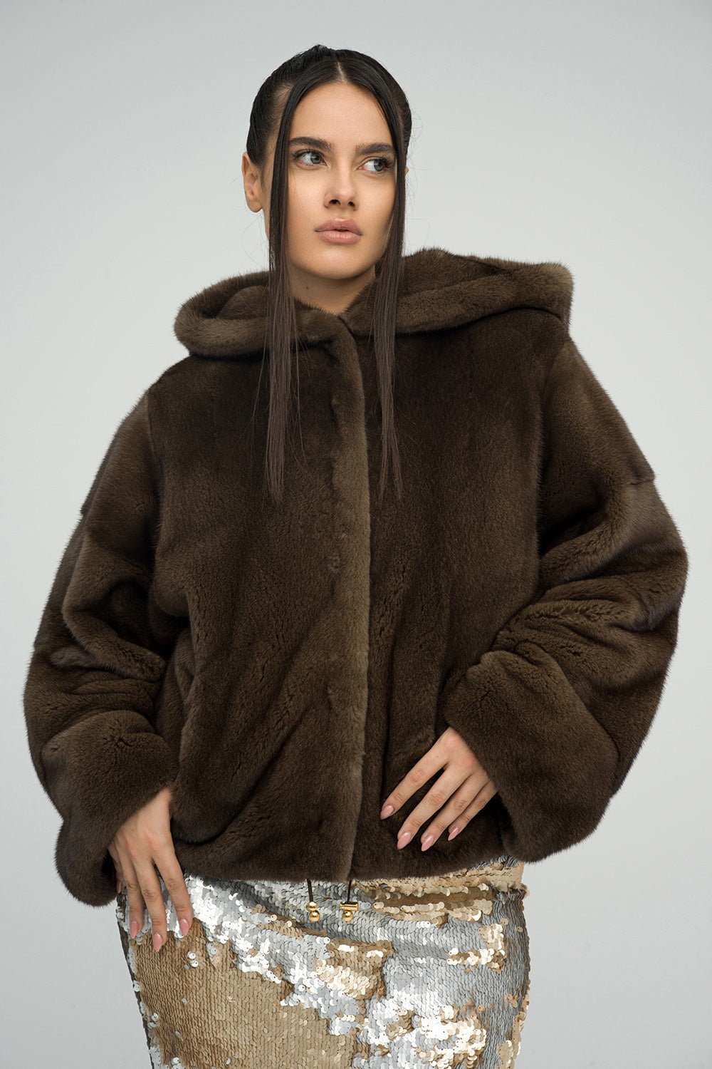 Brown fluffy hooded mink fur coat with a relaxed fit, featuring a button closure and soft texture, paired with a sequined ski