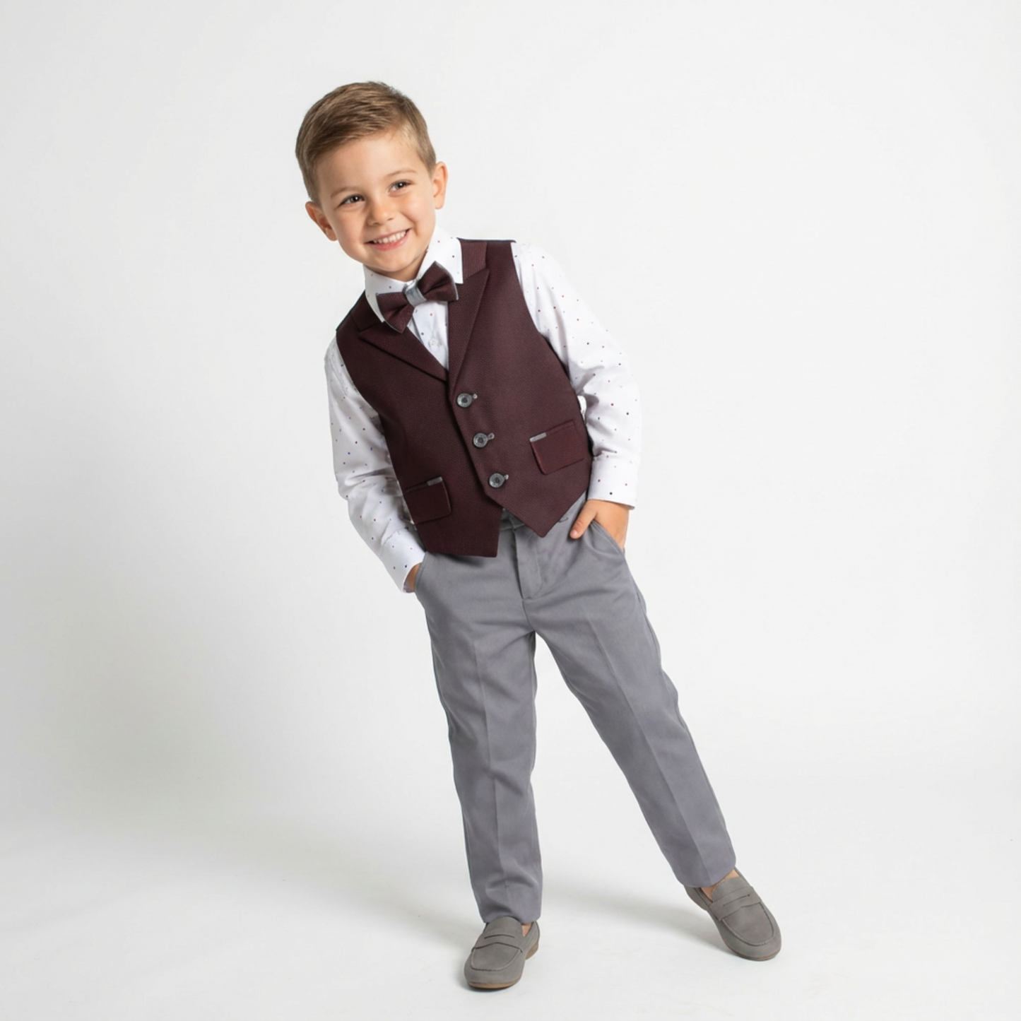 Dapper David Formal Vest Set features a boy in a burgundy vest, white shirt with dots, gray pants, and gray shoes.