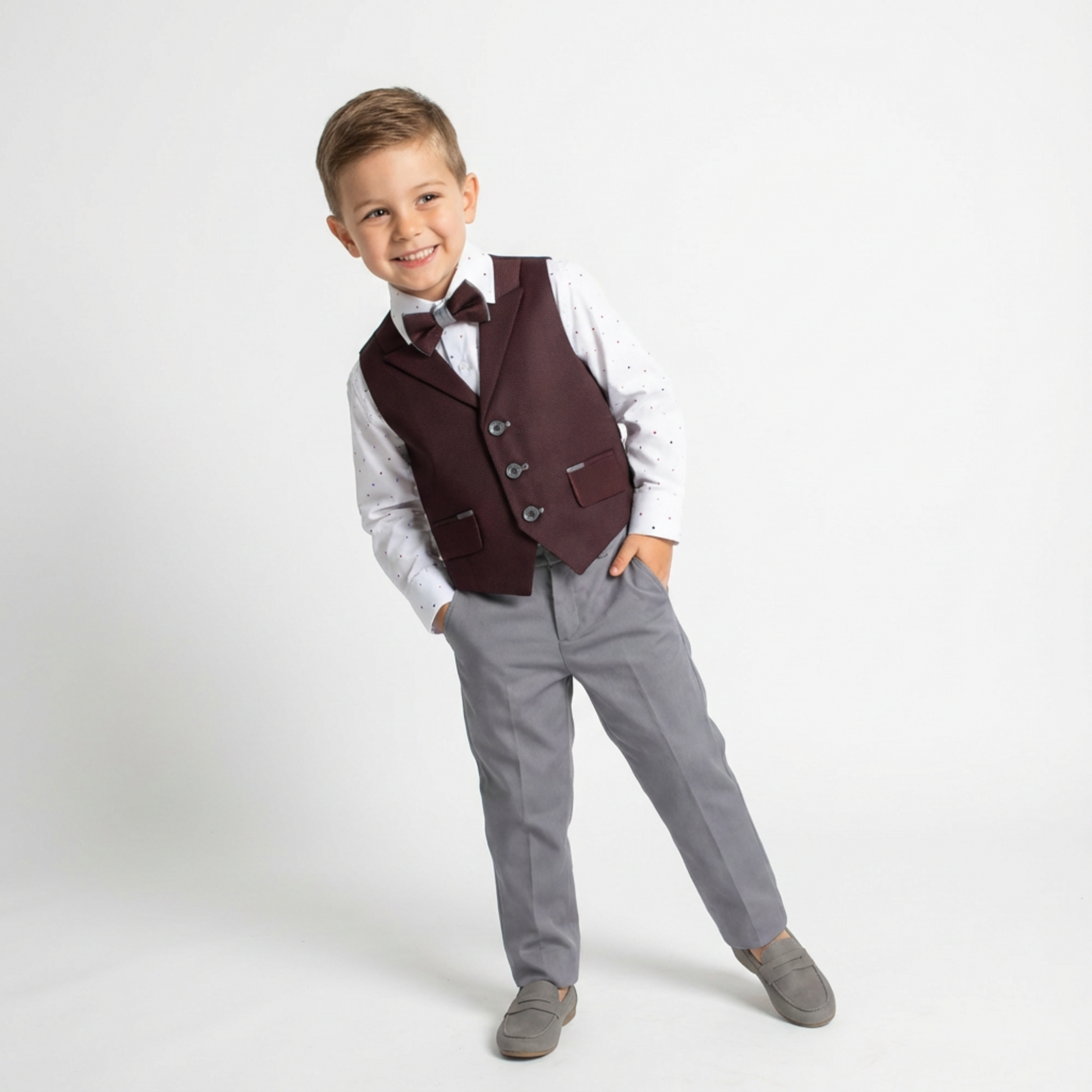 Dapper David Formal Vest Set features a boy in a burgundy vest, white shirt with dots, gray pants, and gray shoes.