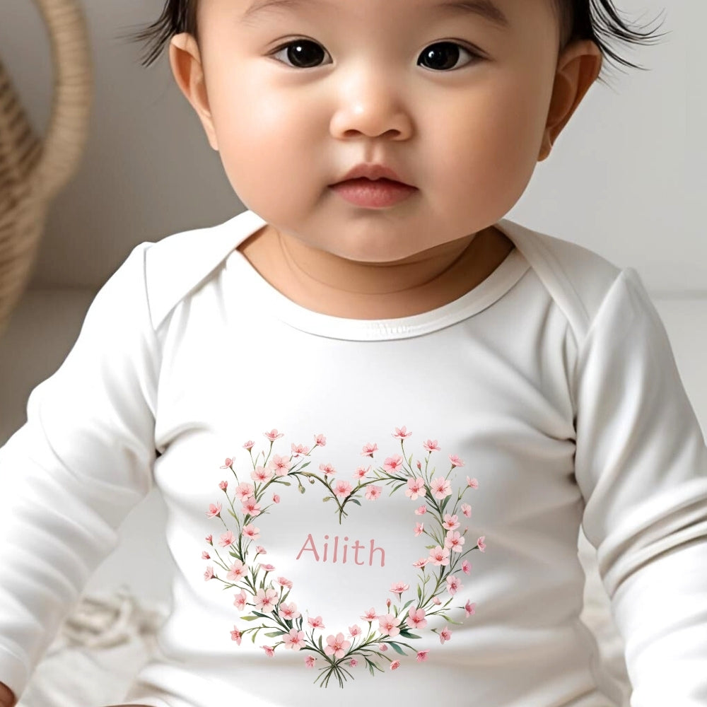Personalised Pink Flower Heart Name Gift Hamper featuring a baby in a white vest with a floral heart design and the name Aili
