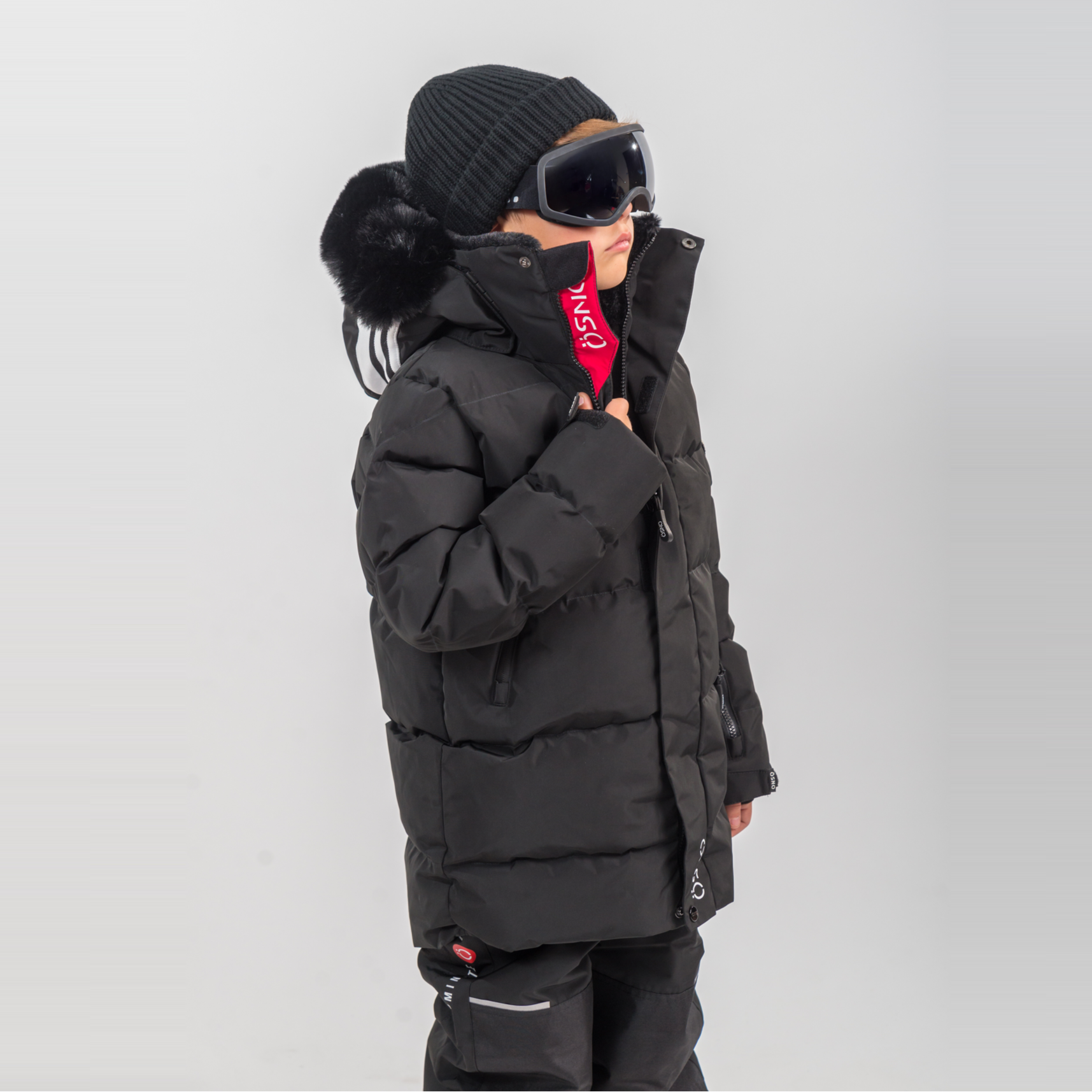 Rafa's Luxury Snowsuit features a black puffy jacket and snowpants, paired with a beanie and oversized goggles.