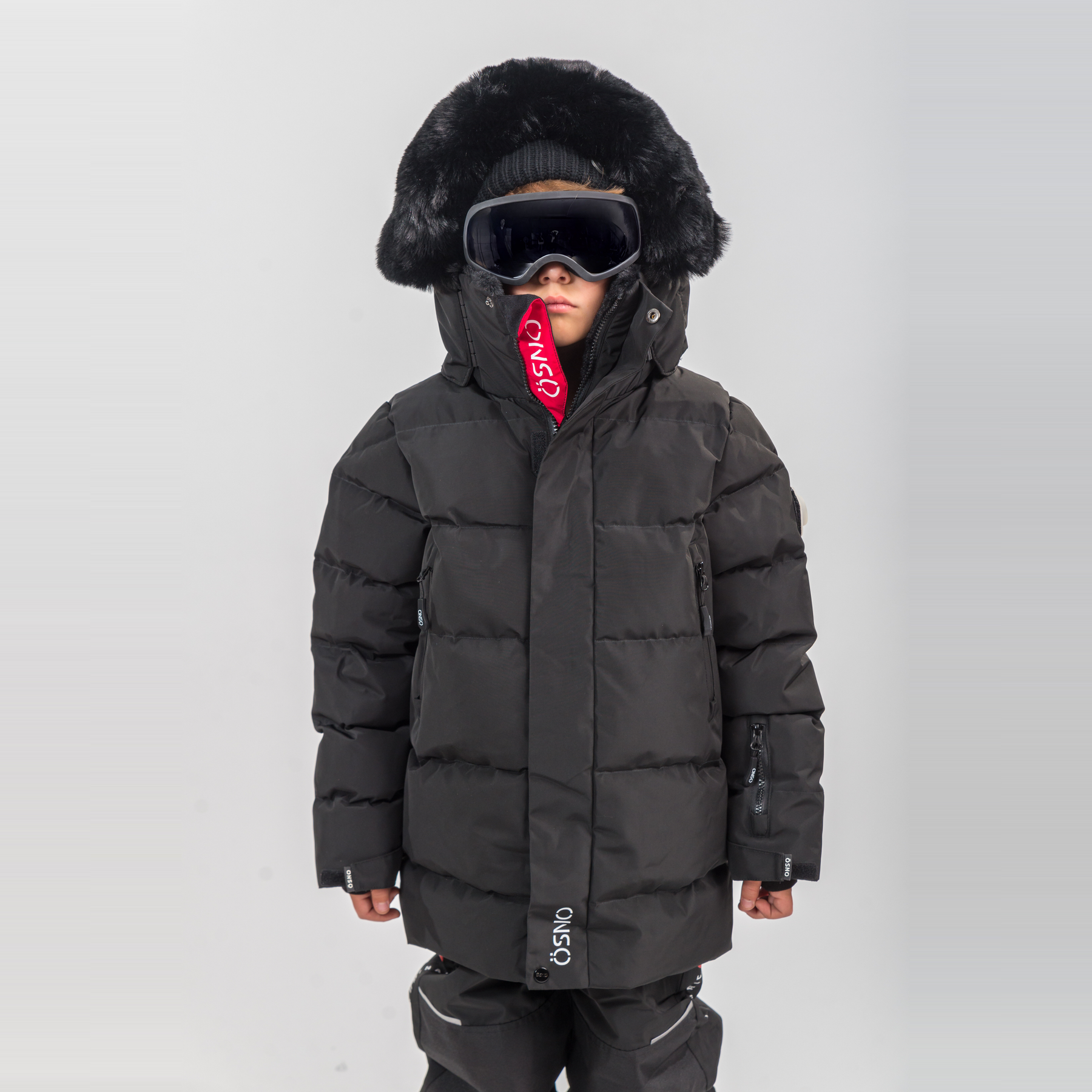 Rafa's Luxury Snowsuit features a black puffer jacket with a fur-lined hood and matching snowpants, worn with goggles.