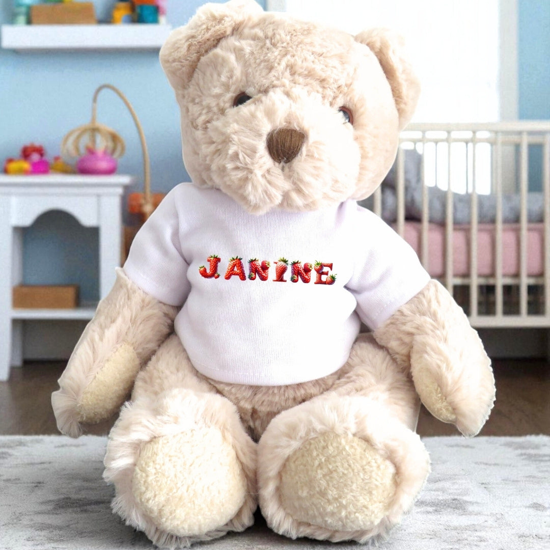 Personalised Strawberry Name Baby Gift Hamper featuring a teddy bear wearing a white vest with the name "JANINE" embroidered.