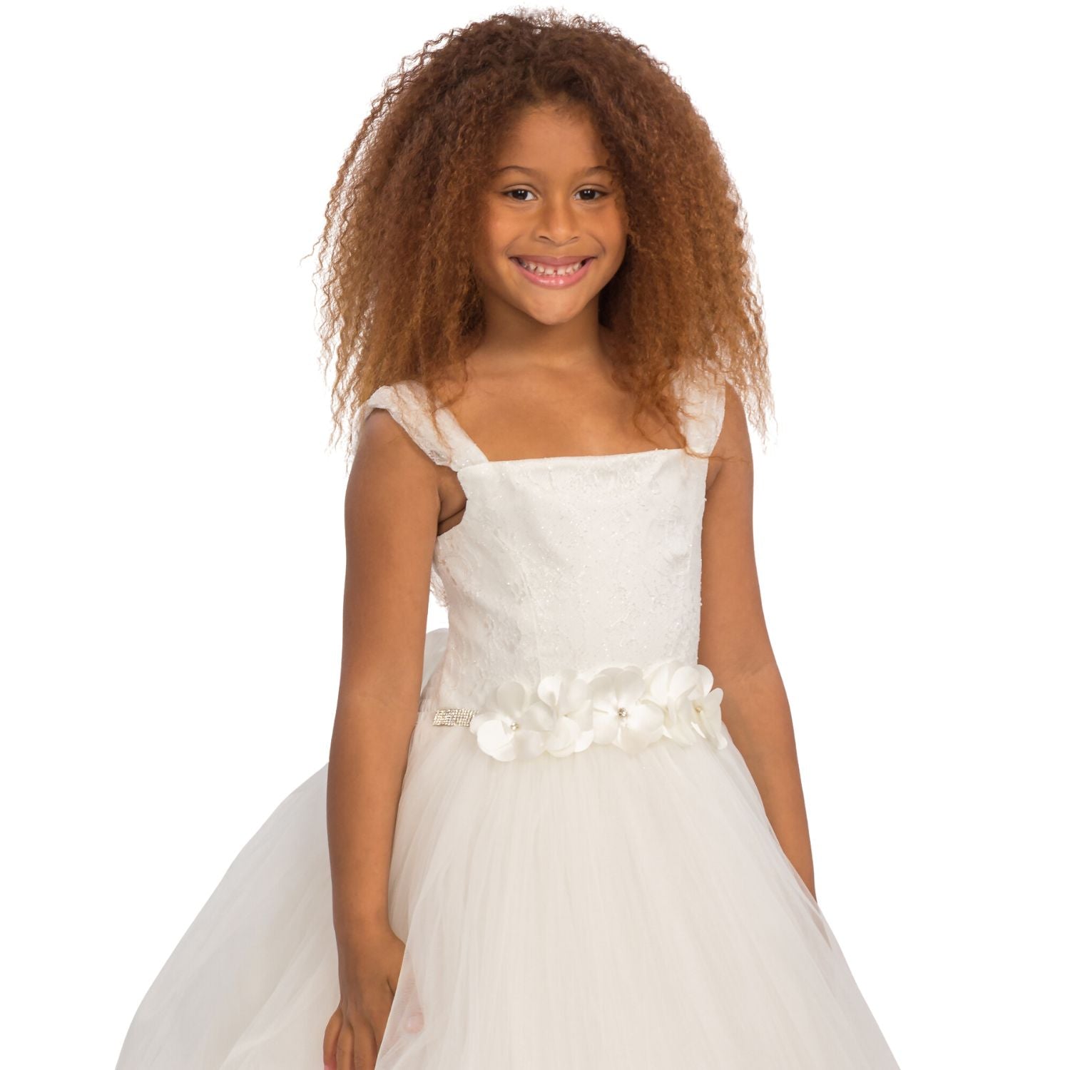 White formal dress for girls featuring a floral belt and tulle skirt, modeled by a smiling girl with curly hair.