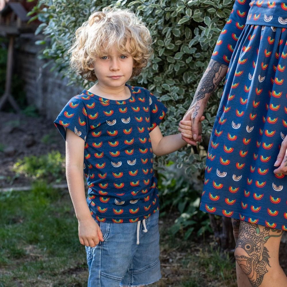 Boob Over the Rainbow Kids top featuring a colorful rainbow pattern, worn by a child holding hands with an adult.