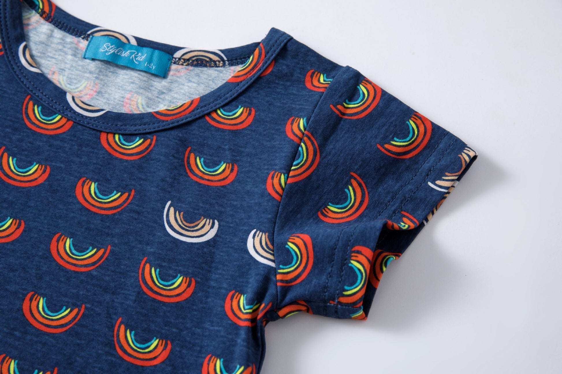Boob Over the Rainbow Kids top featuring a navy background with colorful rainbow patterns and short sleeves.
