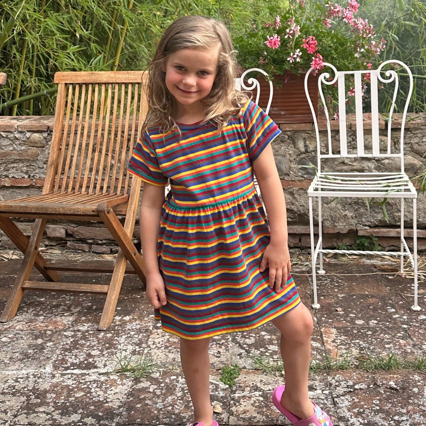 Hazel Rainbow Super Soft Cotton Baby Child Dress featuring colorful stripes, worn by a girl standing outdoors.