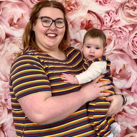 Model wearing a Hazel Stripe Breastfeeding Top with colorful stripes, holding a baby in a matching outfit against a floral ba
