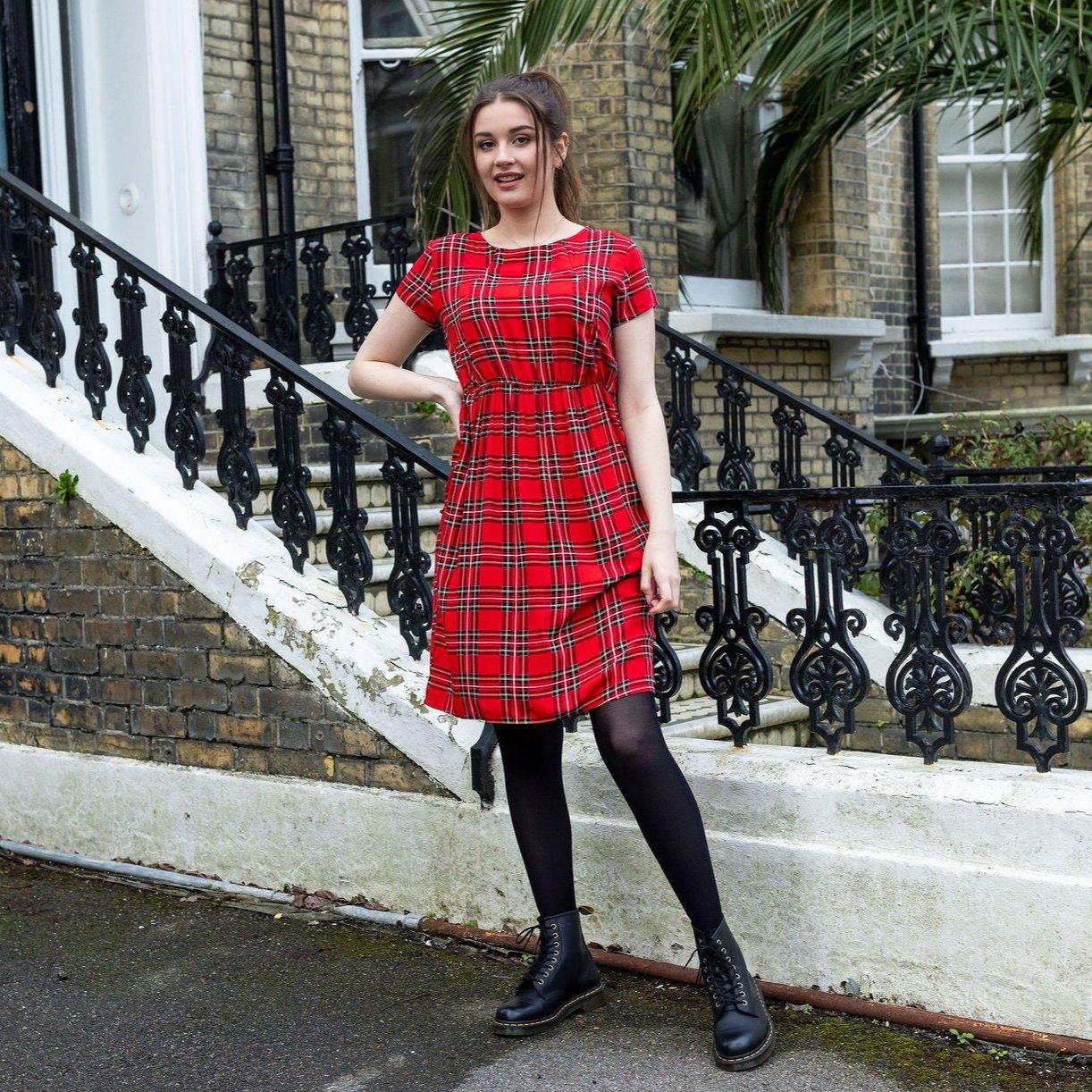 Knee-length red tartan cotton breastfeeding dress, featuring short sleeves and a relaxed fit, styled with black tights and bo